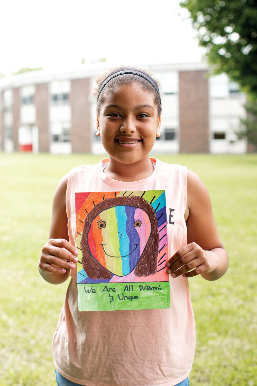 A young girl holding some art, which reads, 'We are all different and unique.'